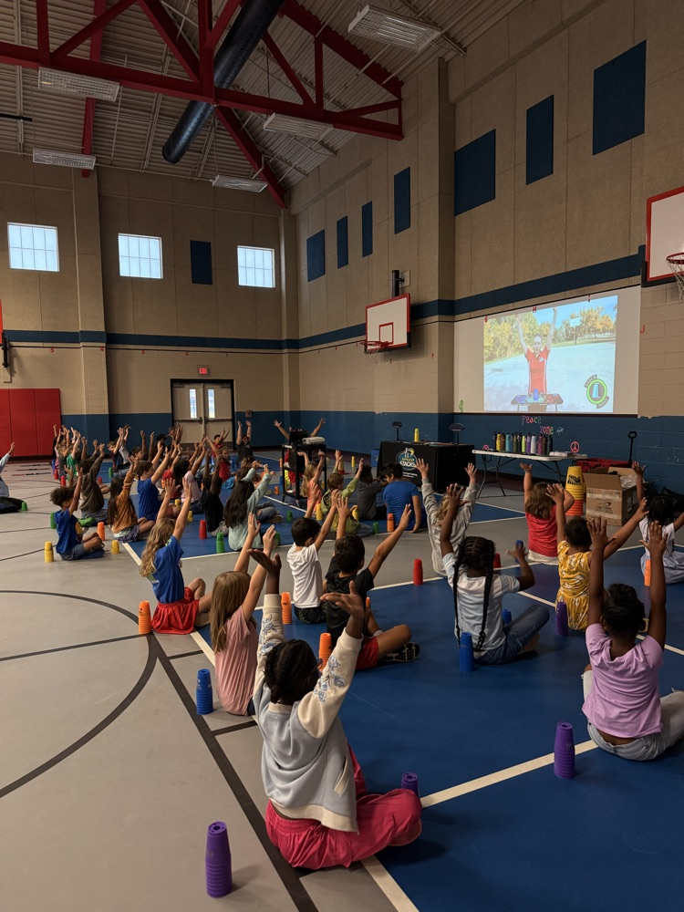 3rd grade students sitting I. PE watching a video on cup stacking.