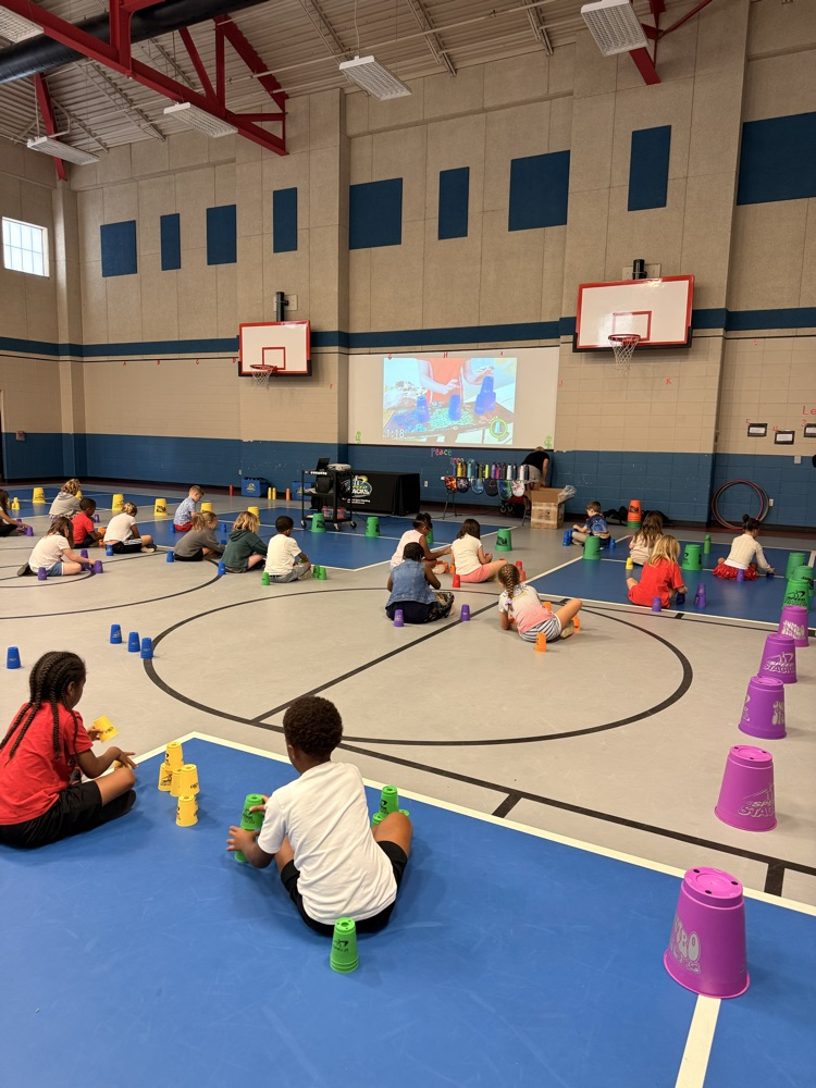 2nd grade students sitting in PE watching a video on cup stacking.