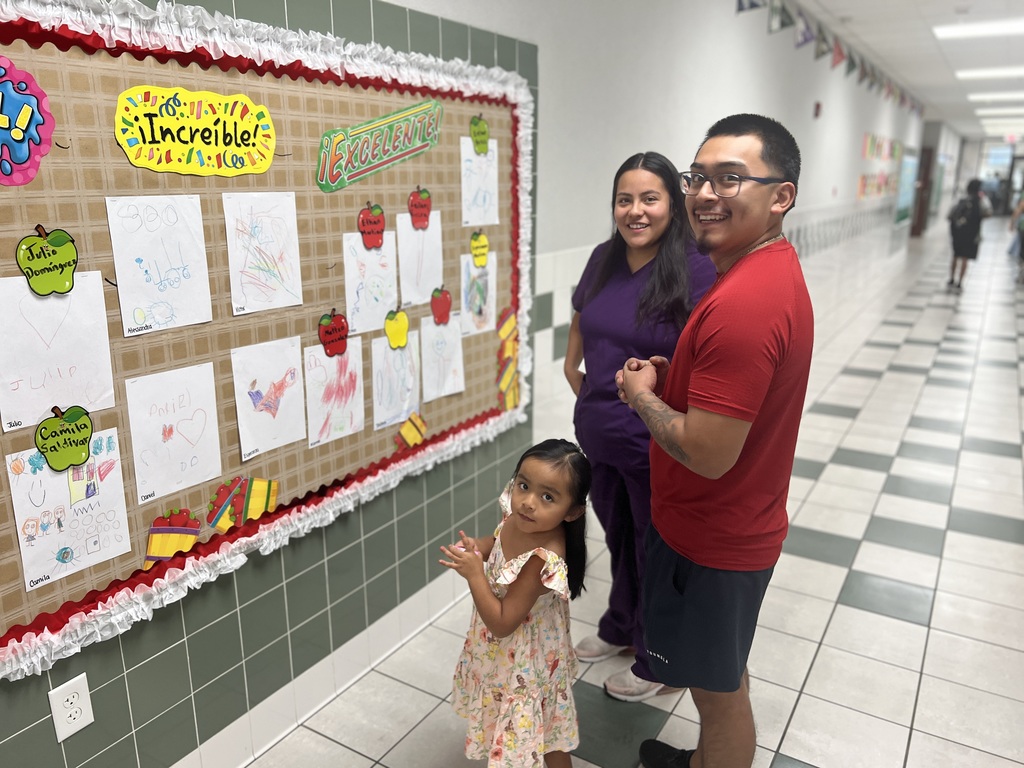 parents and little girl looking at a bulletin board
