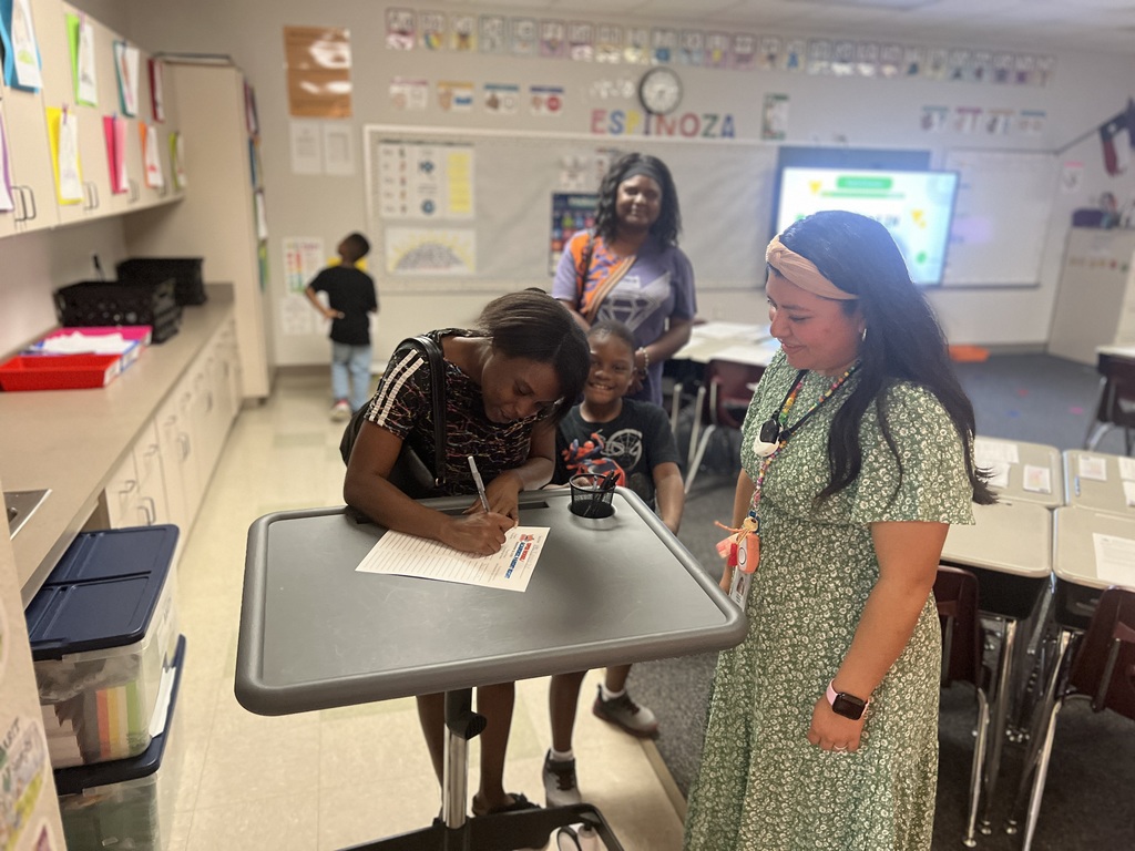 parents signing in on sign in sheet in classroom while teacher watches