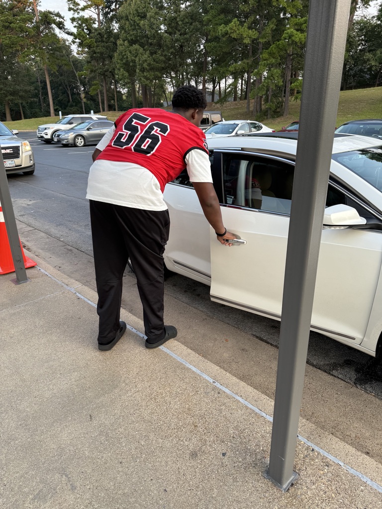 Football player helping students out of cars.