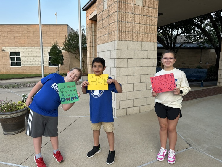 3 students holding signs that say “hello"