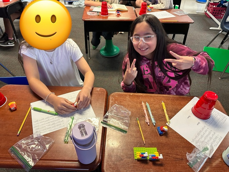 two girls sitting at two desks working with Legos