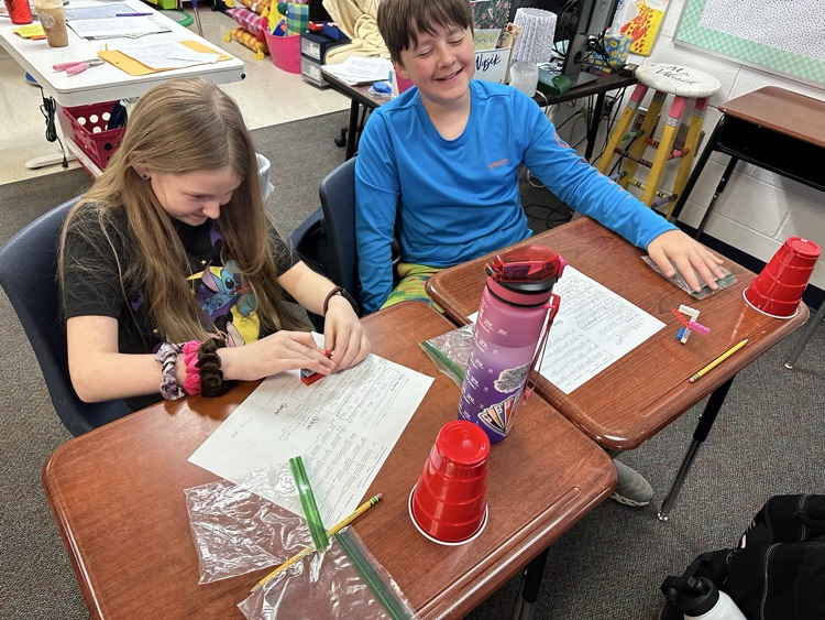 two students sitting at desks working on a Lego project