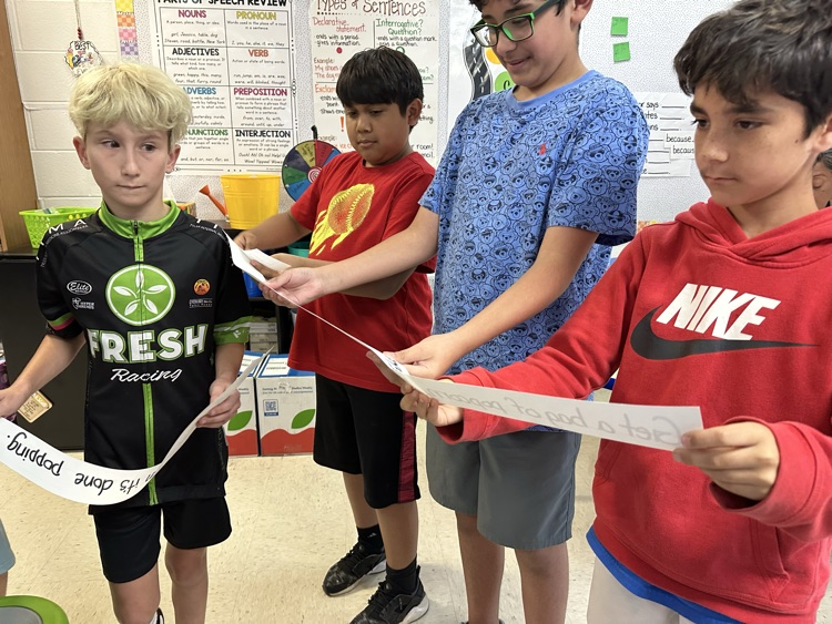 four boys standing in line looking at sentence strips