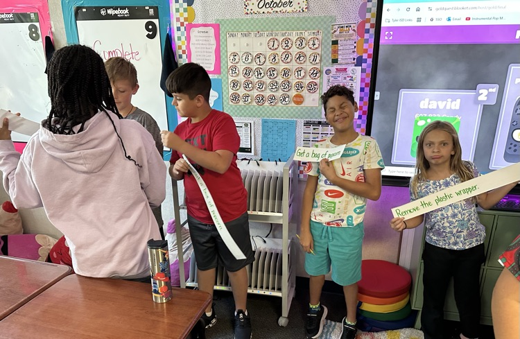 four students standing in the front of class working on a sentence activity