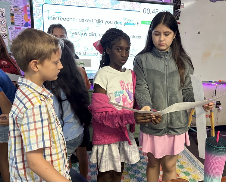 three students standing together organizing sentence strips
