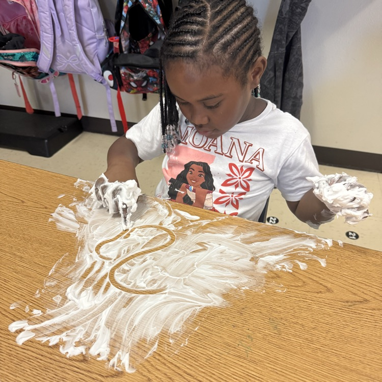 student practicing writing their letters and shaving cream on the table