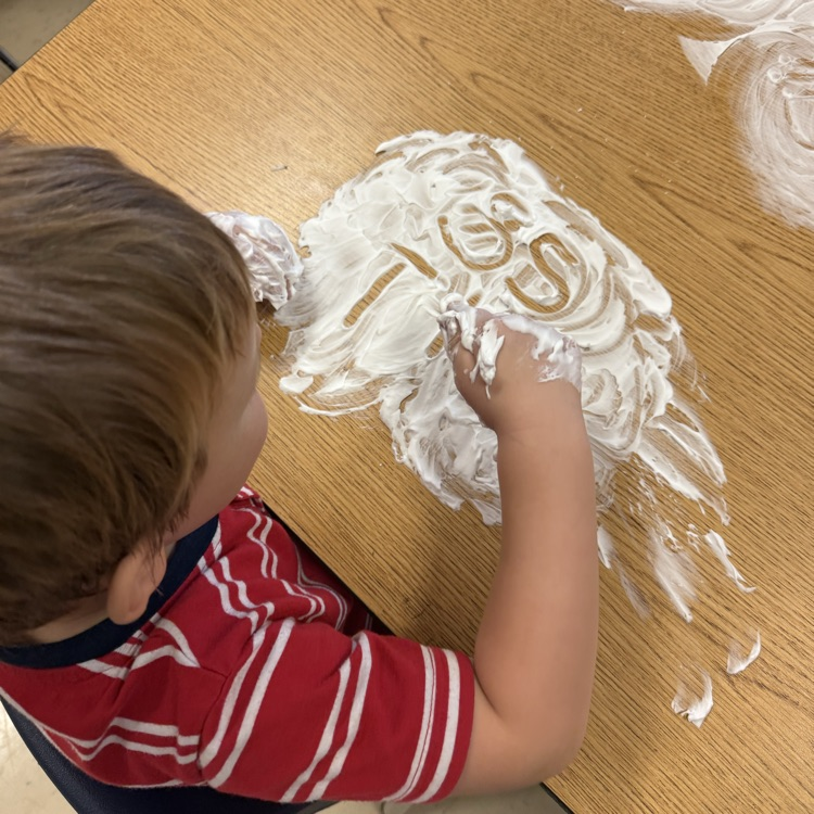 Student practicing writing their letters and shaving cream on the table
