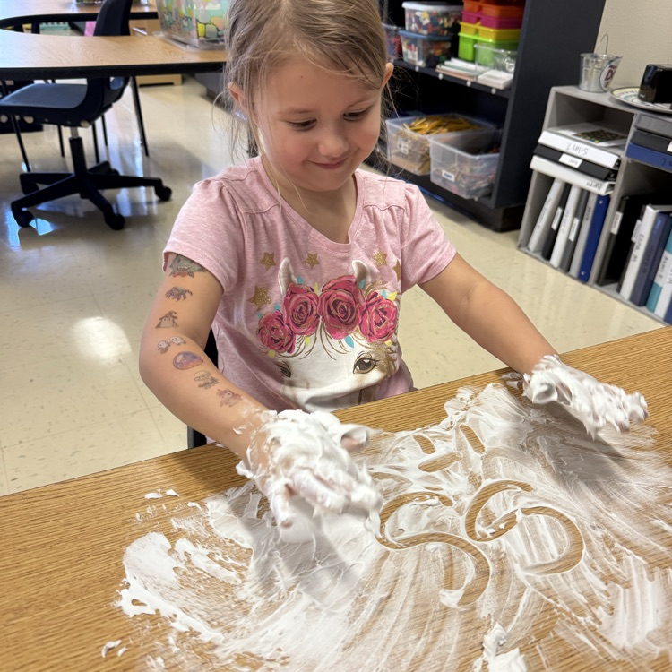 Student practicing writing their letters and shaving cream on the table