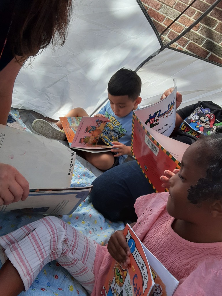 Children reading books while sitting in a tent