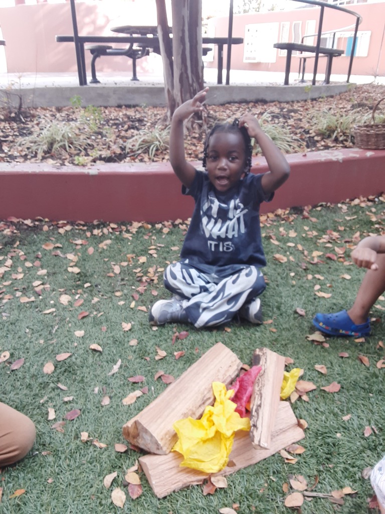 Children sitting on the ground in front of a pretend campfire