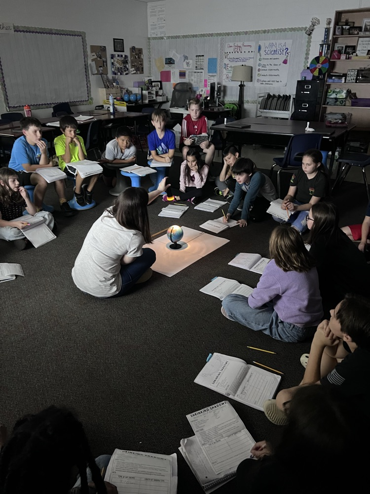 students sitting on the floor of the class watching an experiment about the solar system and light.