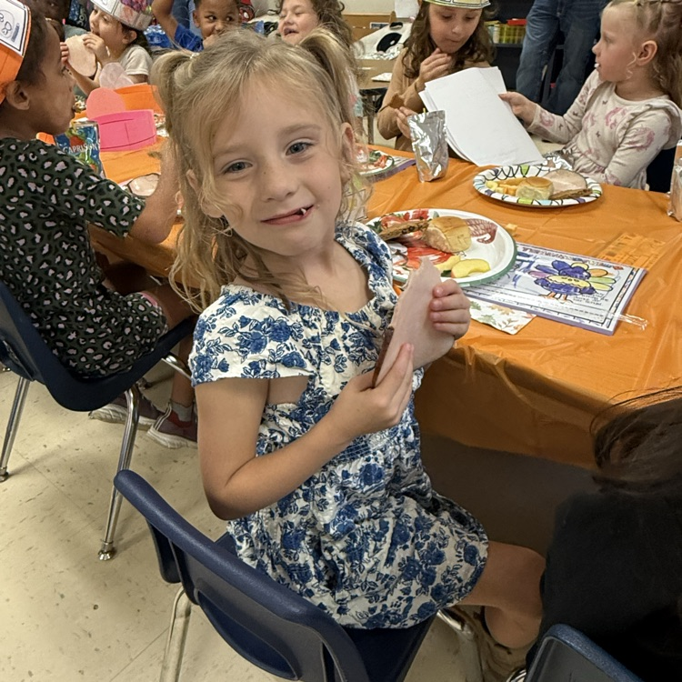 kindergarten students partaking in a Thanksgiving feast at a long table