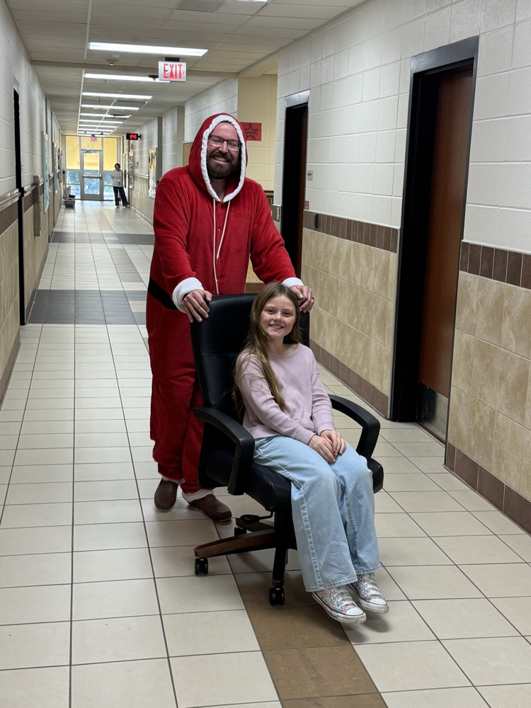 student riding in a desk chair pushed by Mr. Wadle