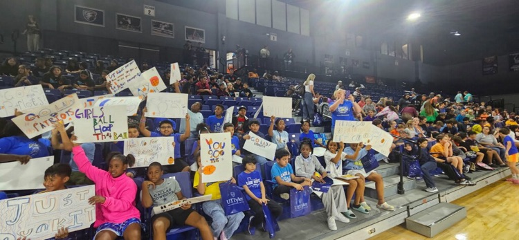 students smiling holding signs at a basketball game