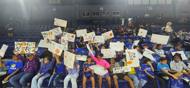 students smiling holding signs at basketball game