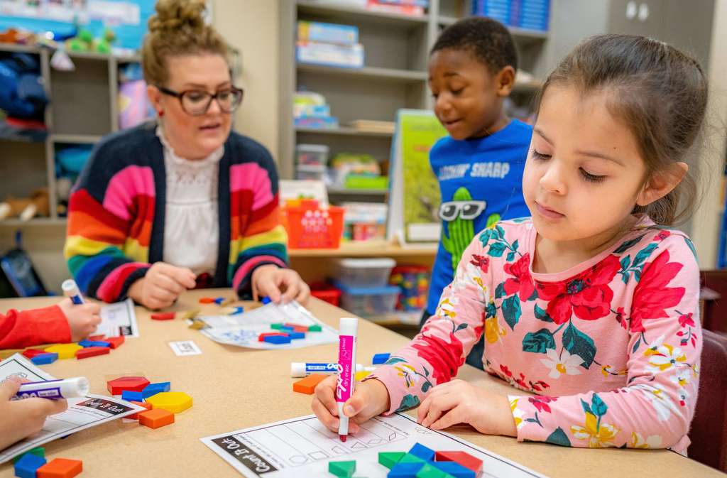 prek students working their teacher at a table with blocks and expo markers
