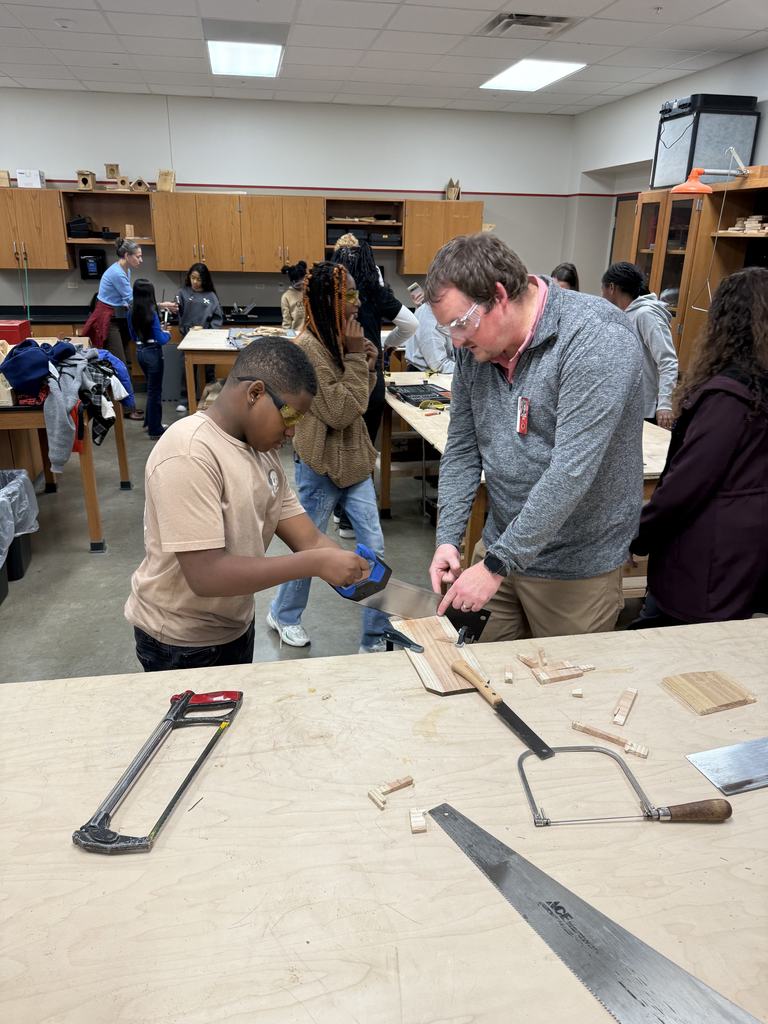 A teacher is helping a boy saw a piece of wood.