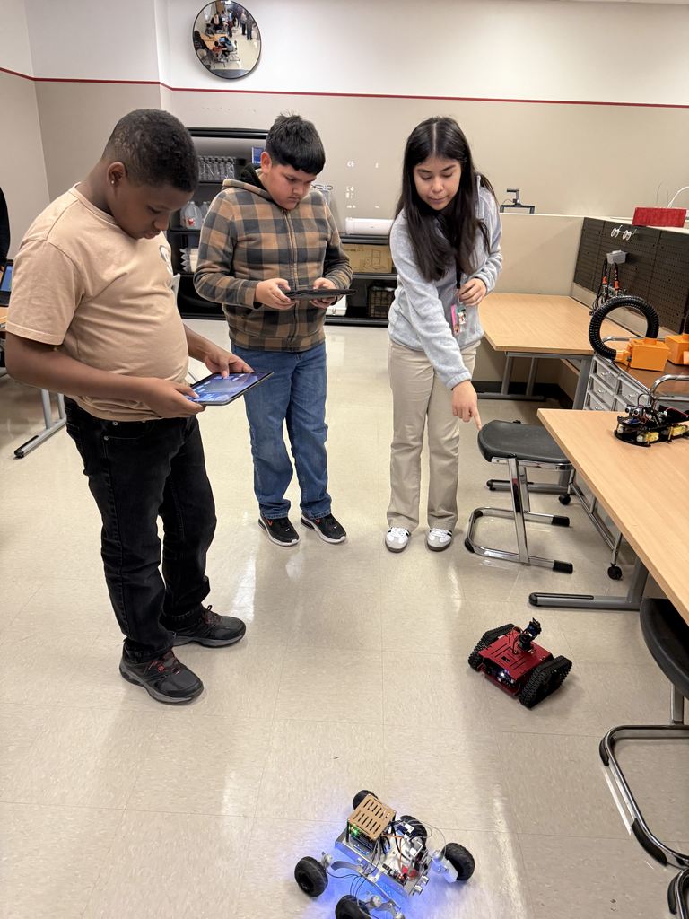 A middle school student is showing two boys how to program two robots.