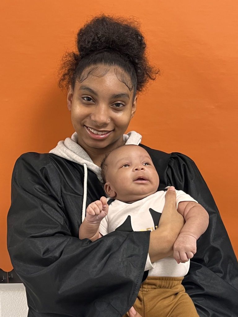 Student posing in graduation regalia w/ her new born