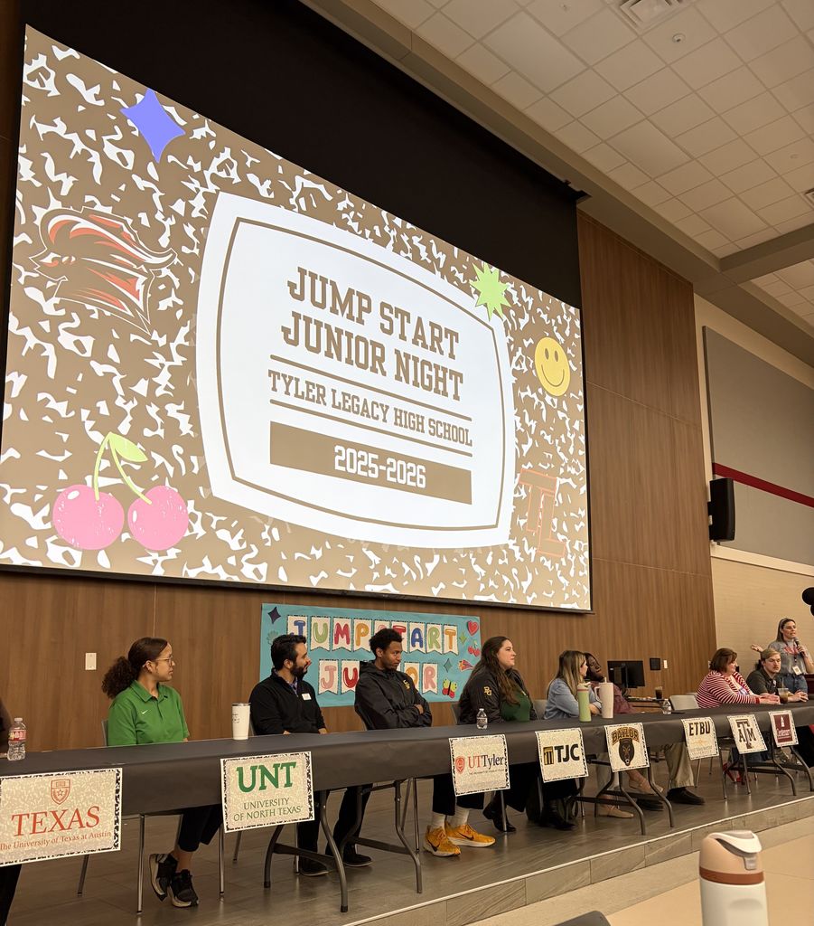 The presenter panel sitting at a long table on stage with their university logo in front of them