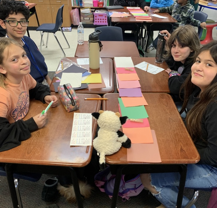 students sitting at a desk using construction paper.