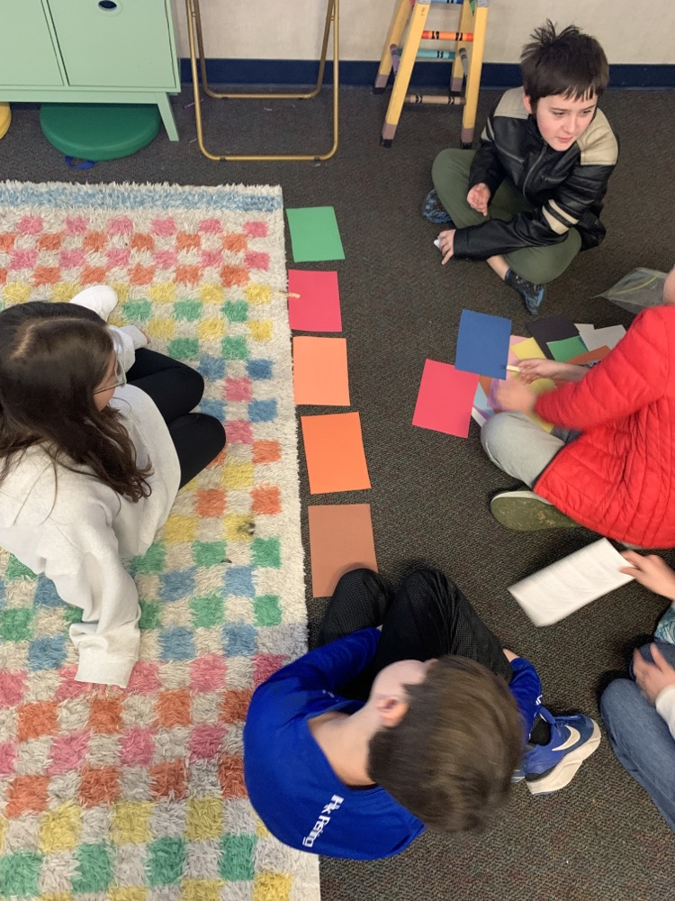 students sitting on the floor completing an activity with construction paper 