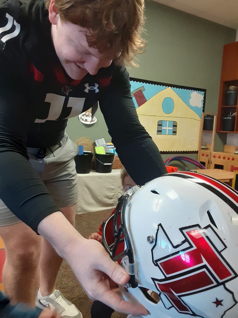 High School football player putting a helmet on a child