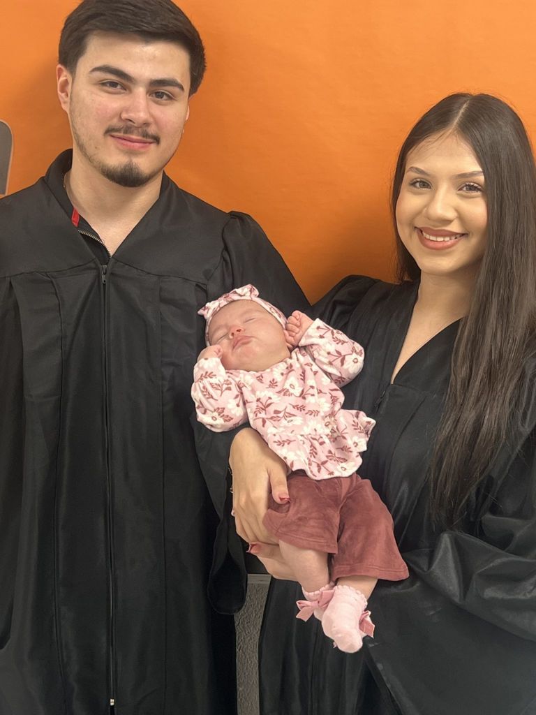 Married Students posing with their newborn in graduation regalia