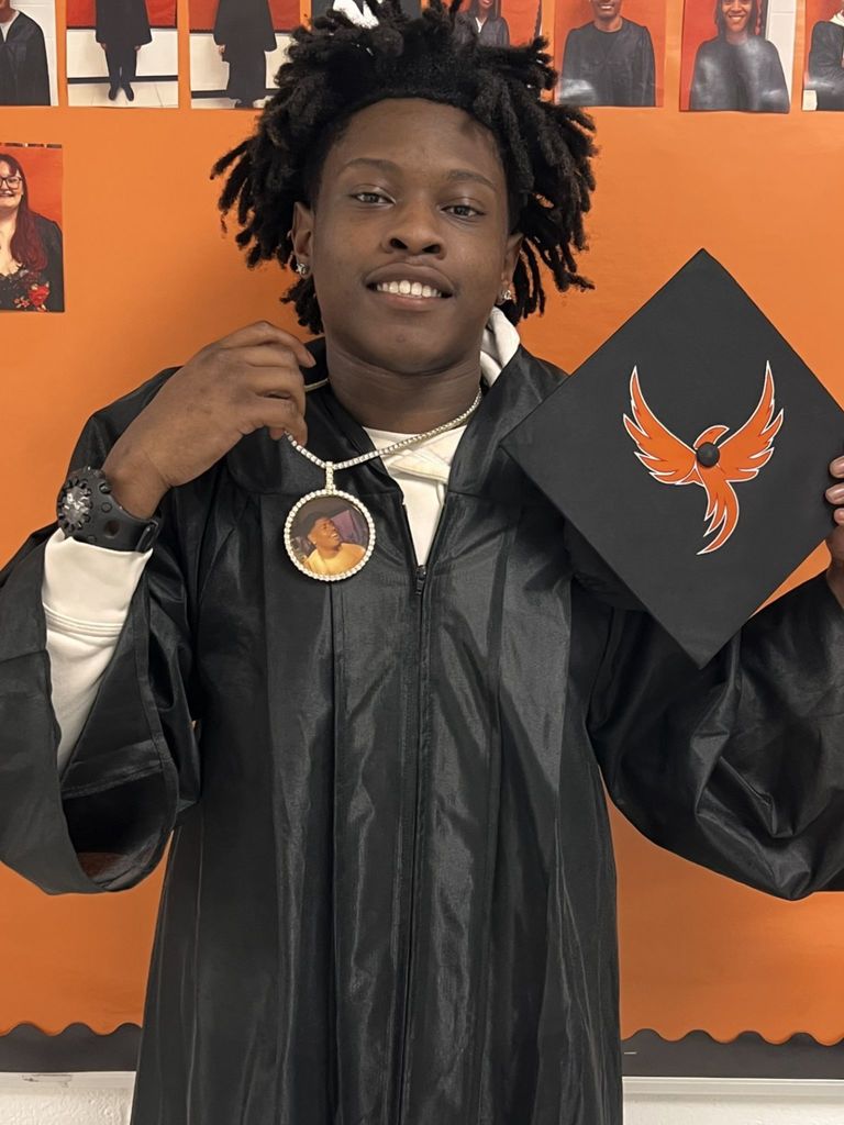 Student posing in graduation regalia holding a chain w/ a relatives image