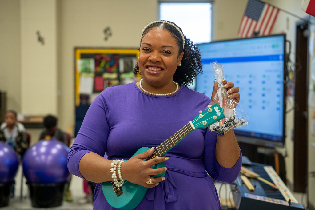 Dixie Music Teacher smiles with blue guitar and holding the WSL appreciation goodie bag.