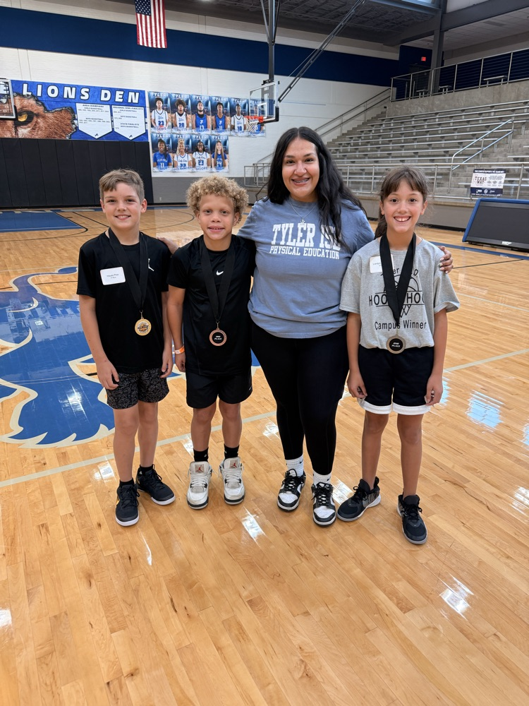 PE coach with three students with medals at a hoop shoot competition in a gym.