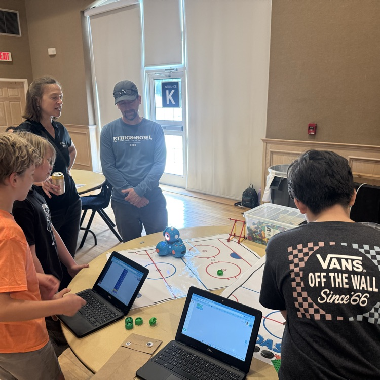 Students coding a robot with a laptop on a hockey mat