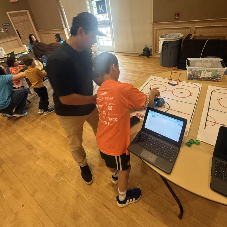 Student and parent coding a robot with a laptop on a hockey mat