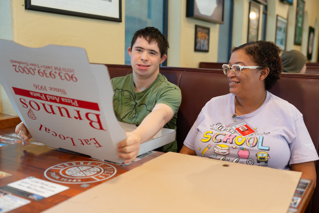 Tyler ISD student smiles and assembles Bruno's pizza boxes next to teacher.