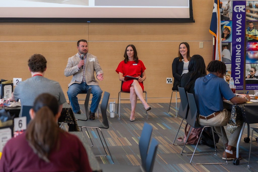 Presenters speak in a room full of students.