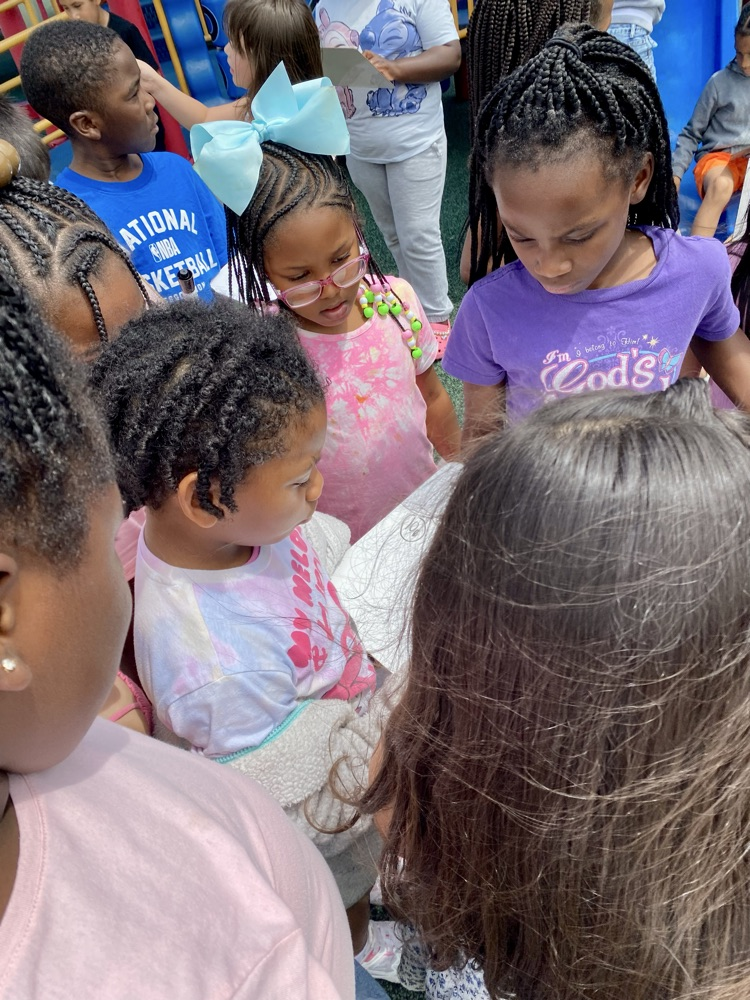 students gathered around another student and listening to student read a clue