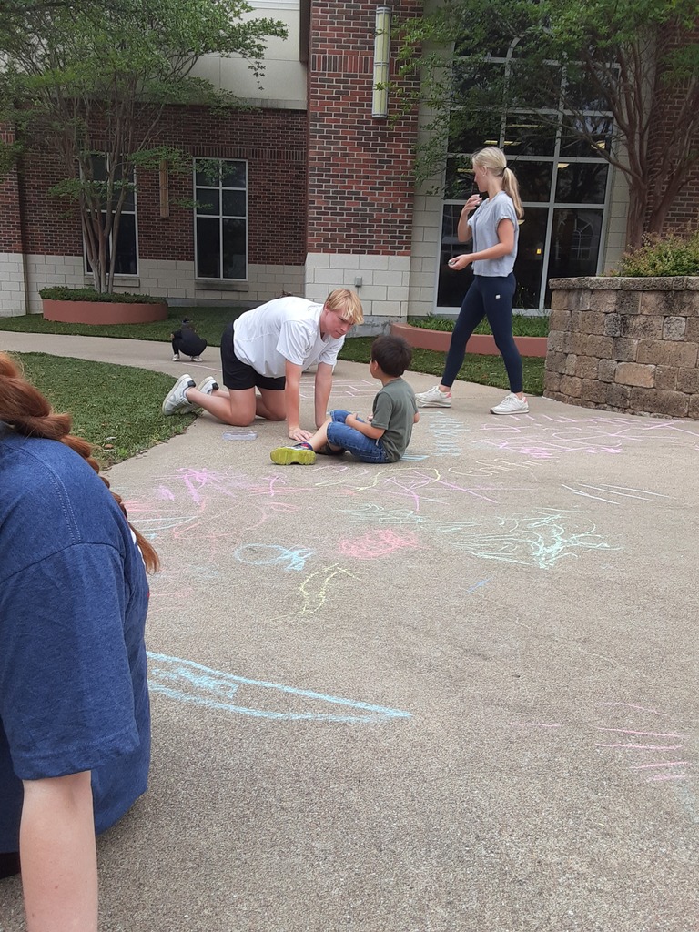 High School students and preschool student using sidewalk chalk