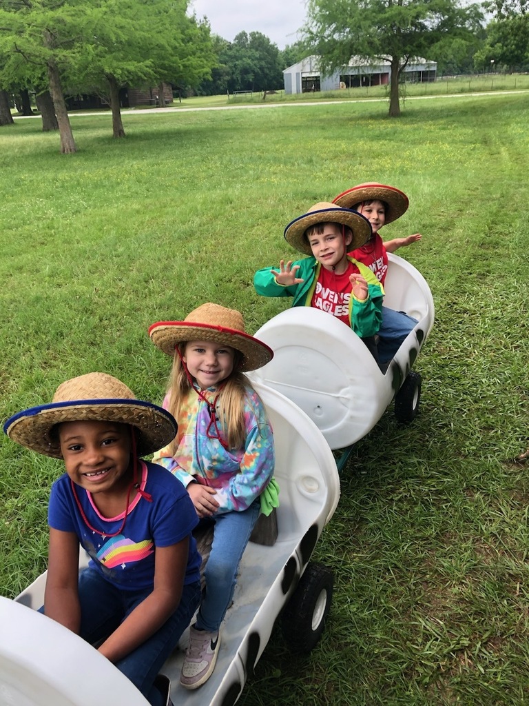 Students on little cars pulled by a tractor.