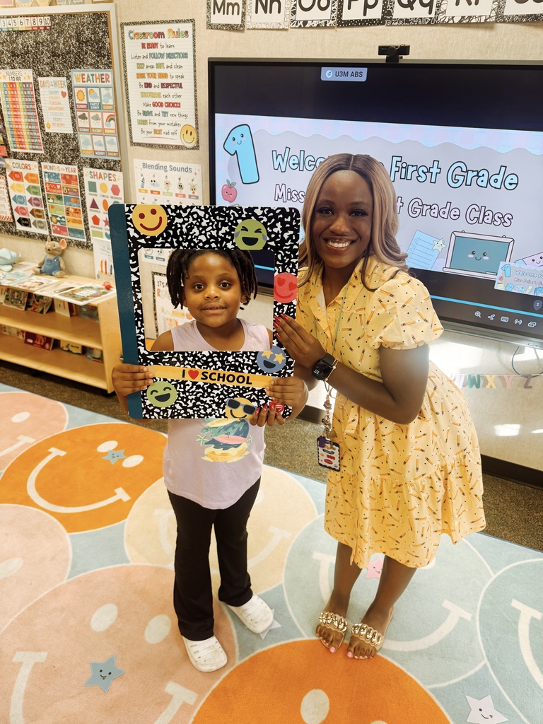 A woman and a young girl stand in front of a screen. The girl holds a photo frame.