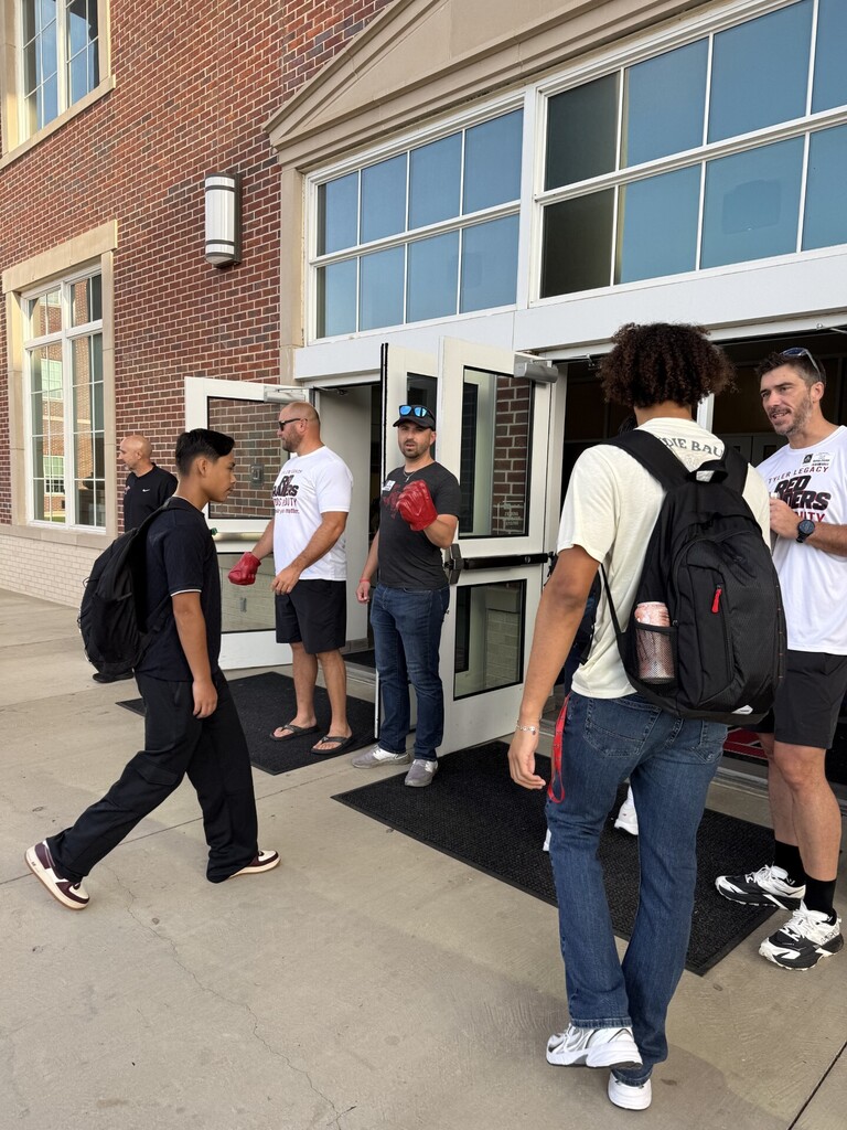 Five people with various clothing and footwear enter a building with brick walls and glass doors.