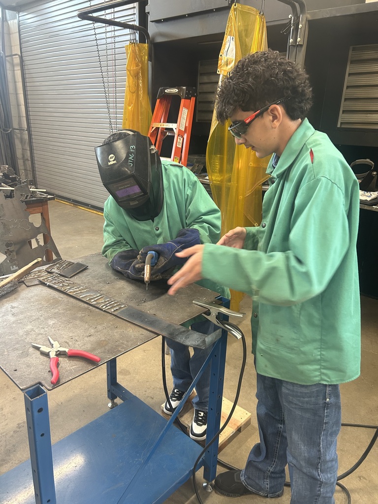 one student helping another student learn how to weld