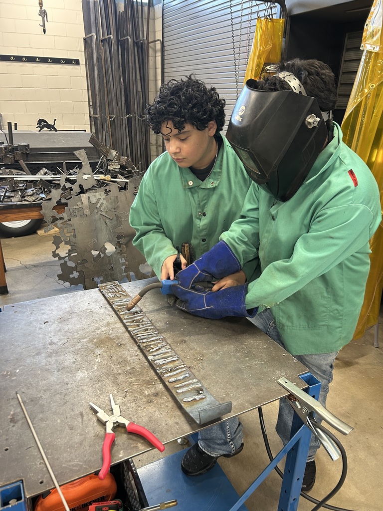 one student teaching another student how to hold a welder