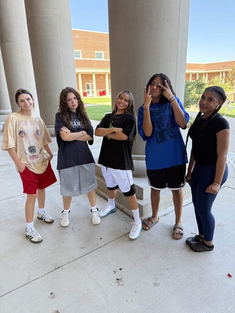 Five people pose in front of pillars. One holds a cellphone to their ear. Behind them is a large building.