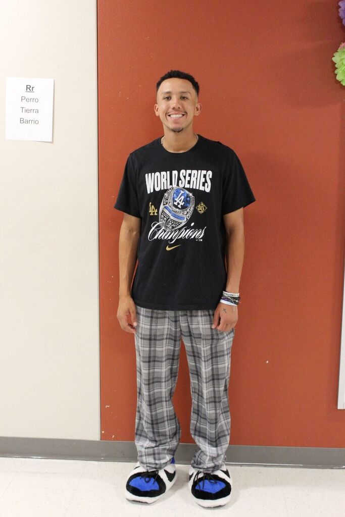 Person in black shirt with "World Series" and California graphic, plaid pants, and sneakers stands against red wall.