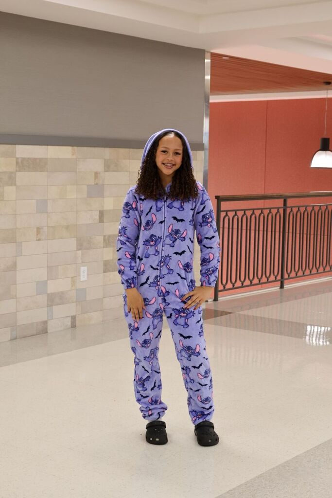 Person in blue bat-themed pajamas standing in a hallway with tiled walls and a metal railing.
