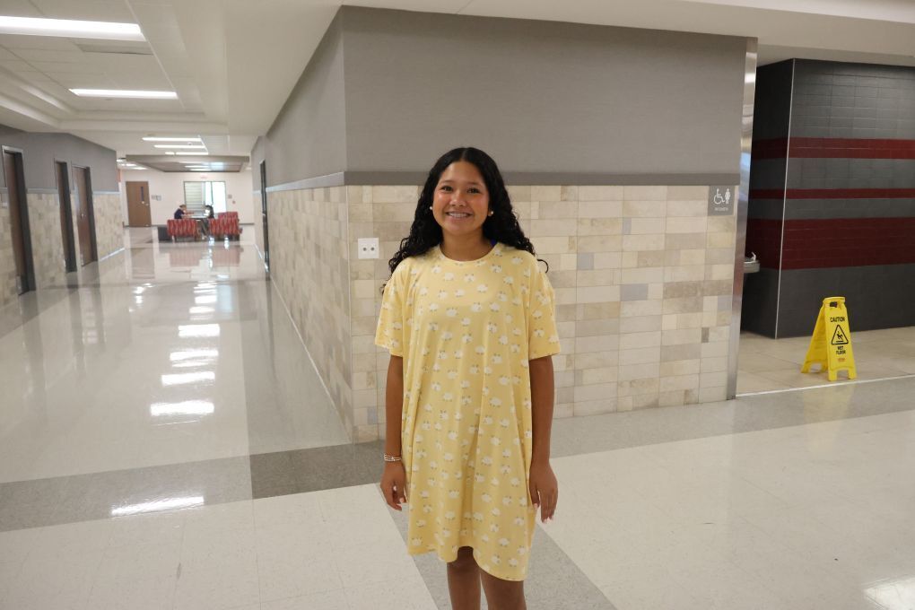 A woman in a yellow dress stands in a hallway with white floors and brick walls.
