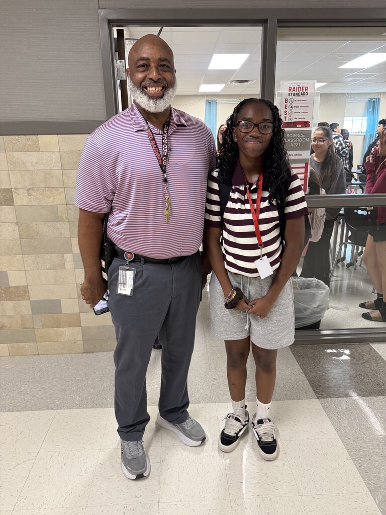 A man and a girl stand next to each other in a school hallway. They both wear IDs.