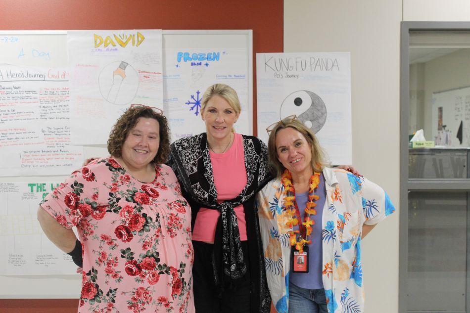 Three women stand next to each other in front of a wall with three posters.